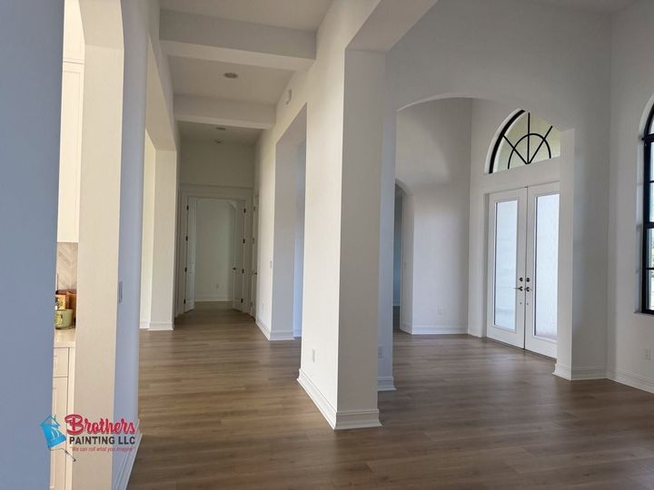 Empty white hallway and living space with wood floors, tall columns, and arched windows.