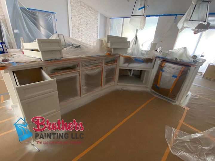 Kitchen cabinets masked for painting in a room covered with plastic sheeting.