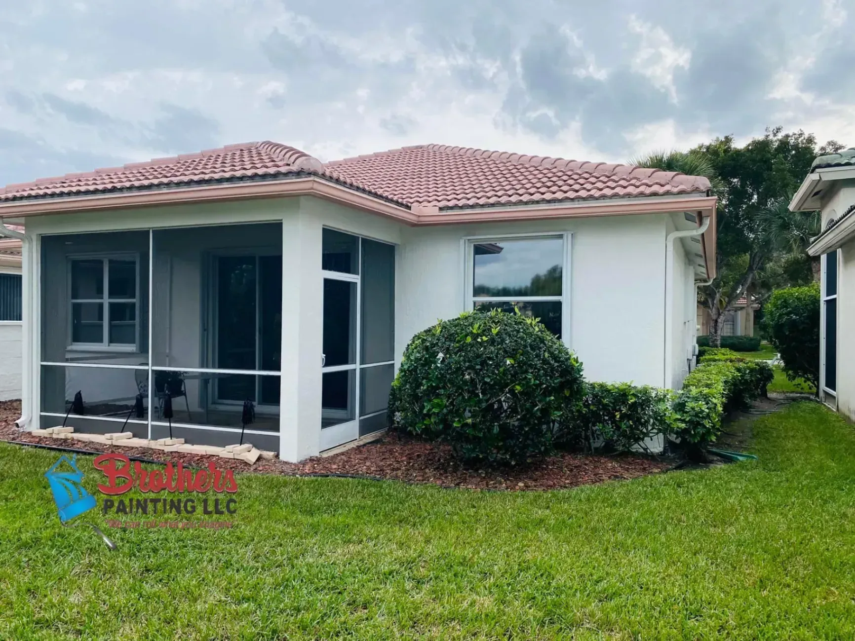 Single-story white house with red tile roof and screened porch, set on a green lawn.
