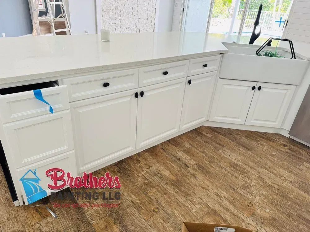 White kitchen cabinets with countertop, sink, and wood-look floor in a bright room