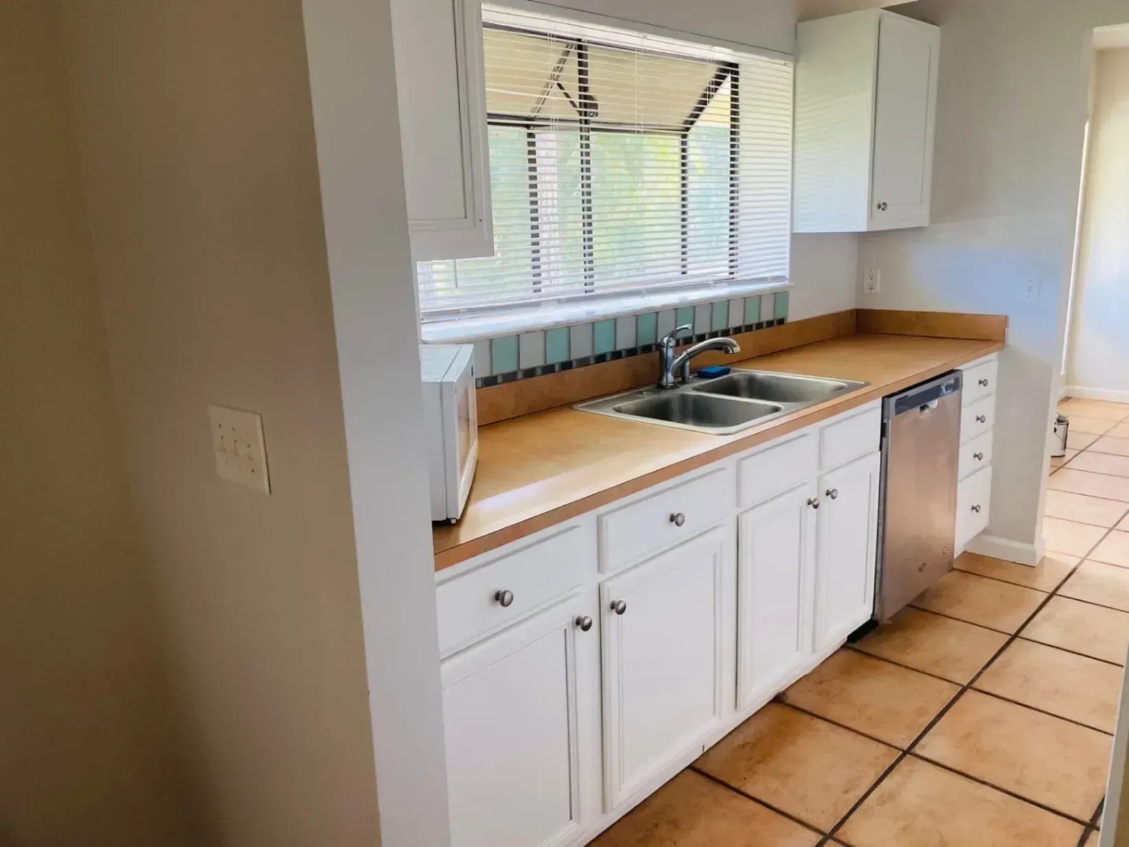 Bright kitchen with white cabinets, wood countertops, sink, dishwasher, and tiled floor.