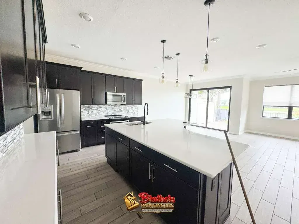 Modern kitchen with dark cabinets, large island, white tile floor, and sliding glass doors.