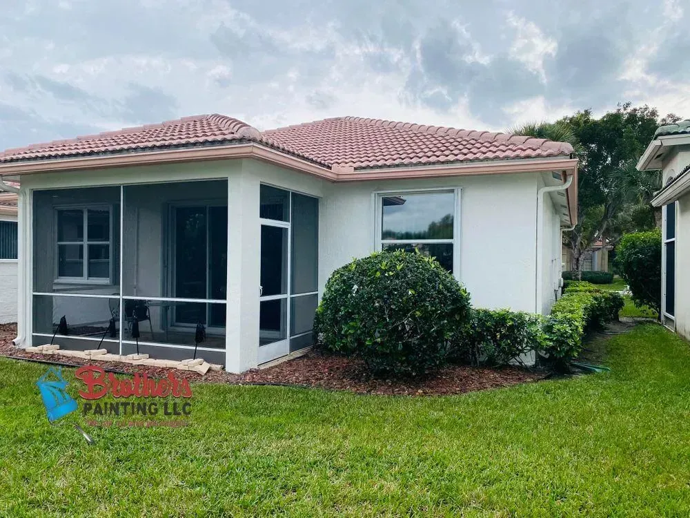 Single-story house with screened porch, pink tile roof, white walls, and a green lawn.