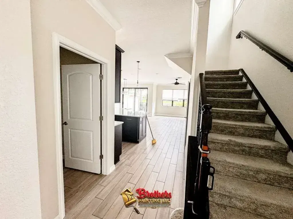 Narrow hallway with white walls, dark wood floor, staircase, and a doorway to a kitchen or living area.