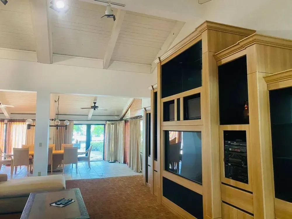 Empty living room with built-in wood entertainment center and vaulted ceiling, lit by daylight.
