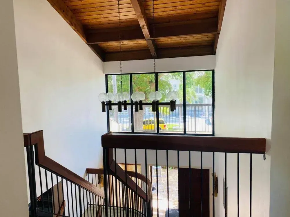 Interior stair landing with white walls, wood ceiling, black railing, and a window overlooking outside.