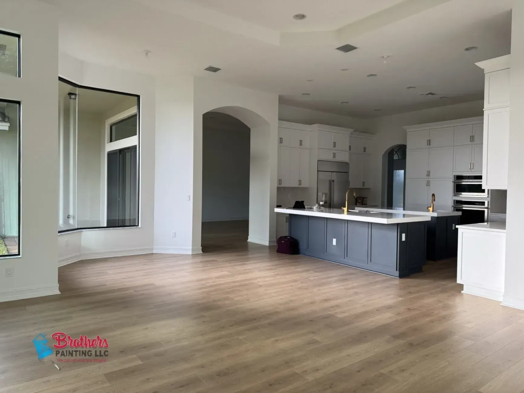 Empty modern kitchen and living area with white walls, wood floors, and a gray island.