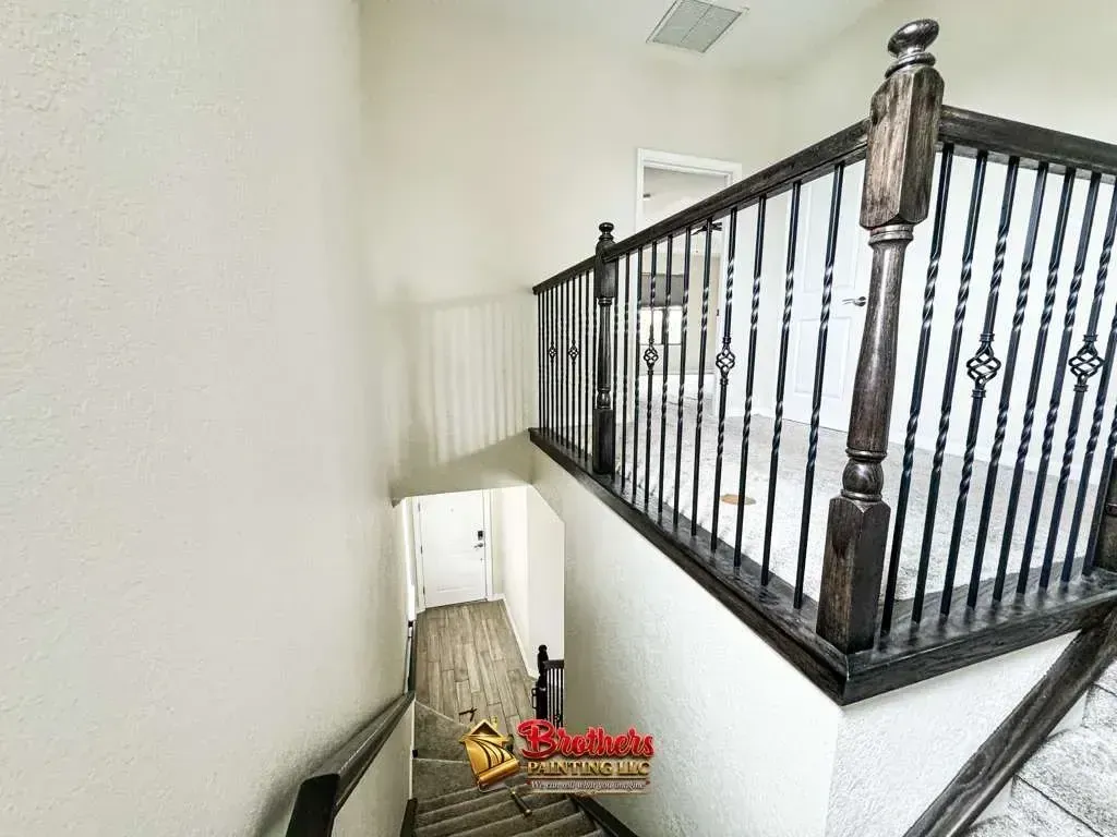 Staircase landing with black metal railing overlooking a narrow stairwell and white walls.