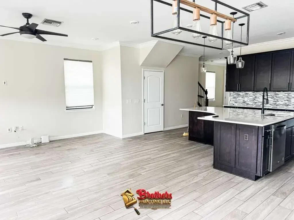 Open-concept kitchen and living room with light wood floors, dark cabinets, and a ceiling fan
