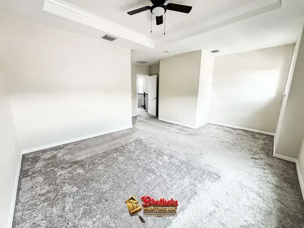 Empty bedroom with gray carpet, white walls, ceiling fan, and walk-in closet opening