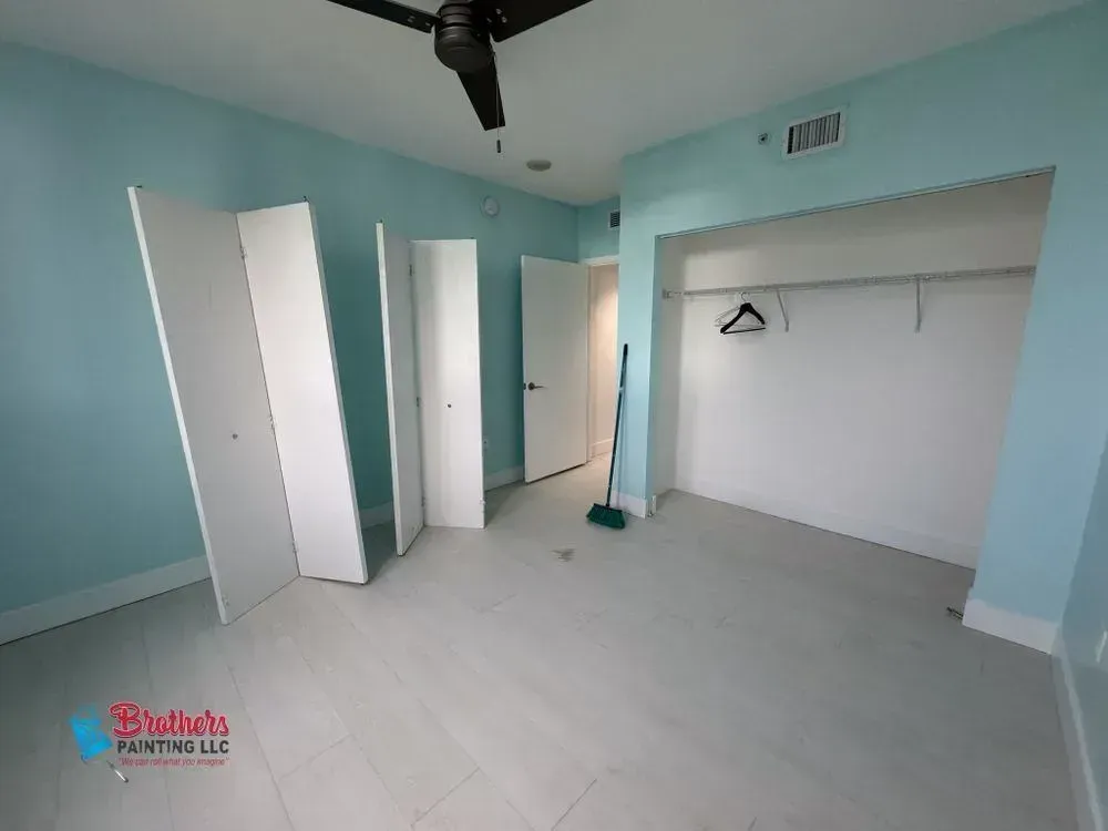Empty light blue bedroom with white closet doors, white tile floor, and ceiling fan.