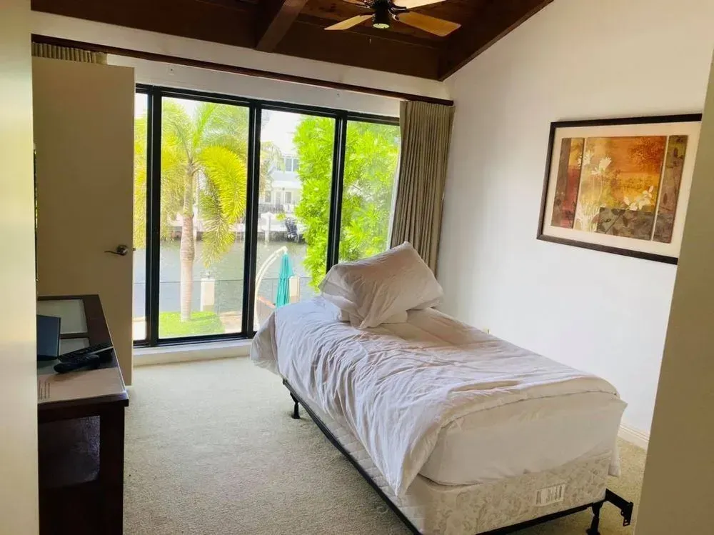 Bedroom with a single bed beside large windows, showing a bright tropical outdoor view.