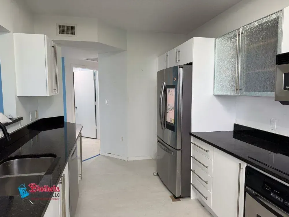 Modern white kitchen with black countertops, stainless appliances, and a hallway in the background