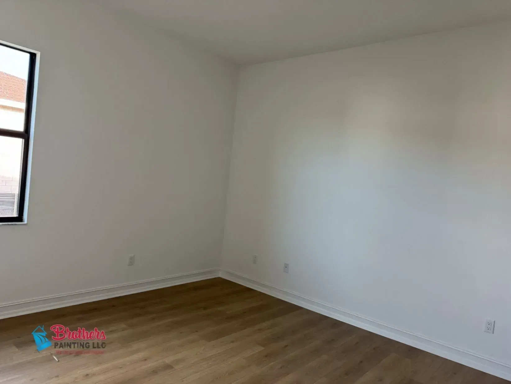 Empty white room with wood flooring and a small window on the left wall