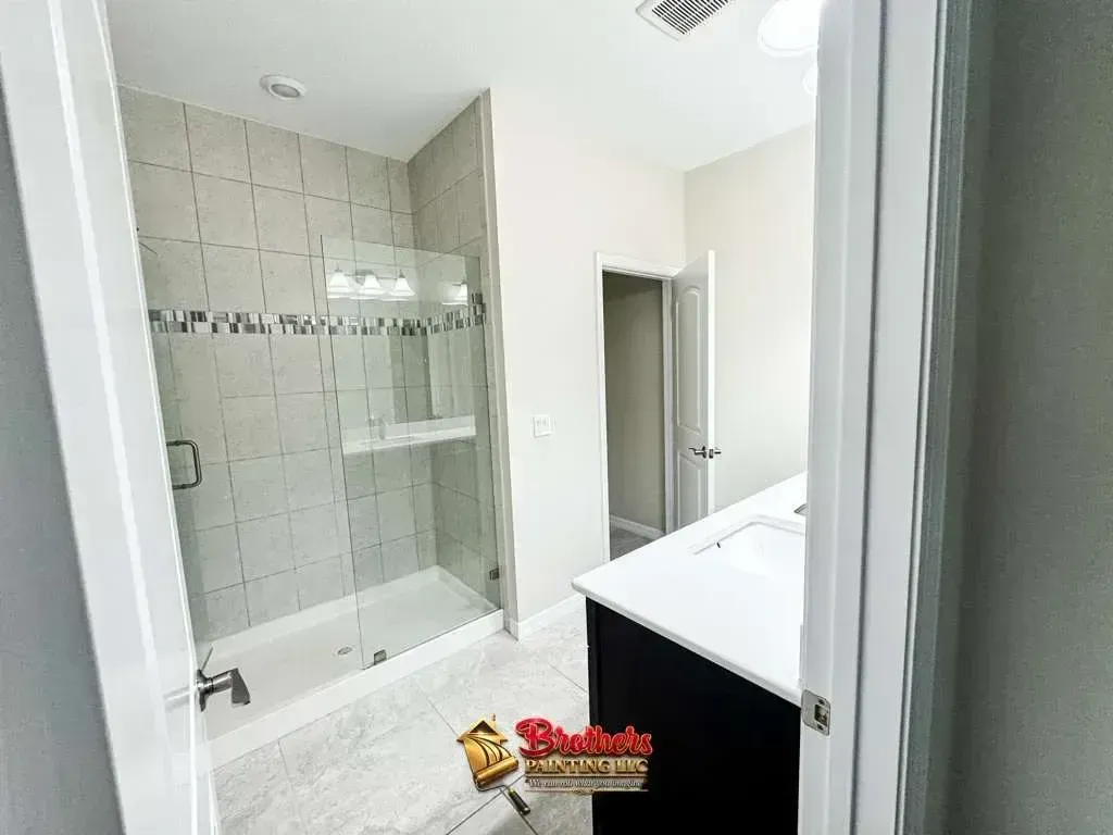 Bright modern bathroom with walk-in glass shower, white vanity, and gray tile walls.