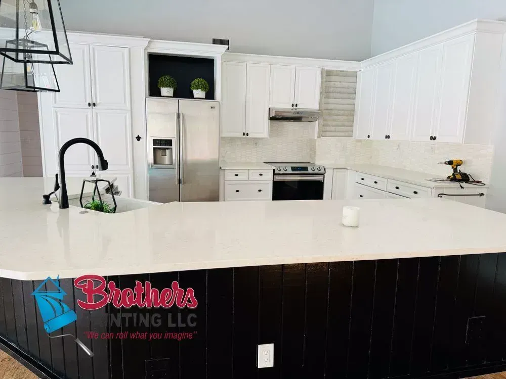 Bright white kitchen with stainless steel appliances, black island, and pendant light over a countertop