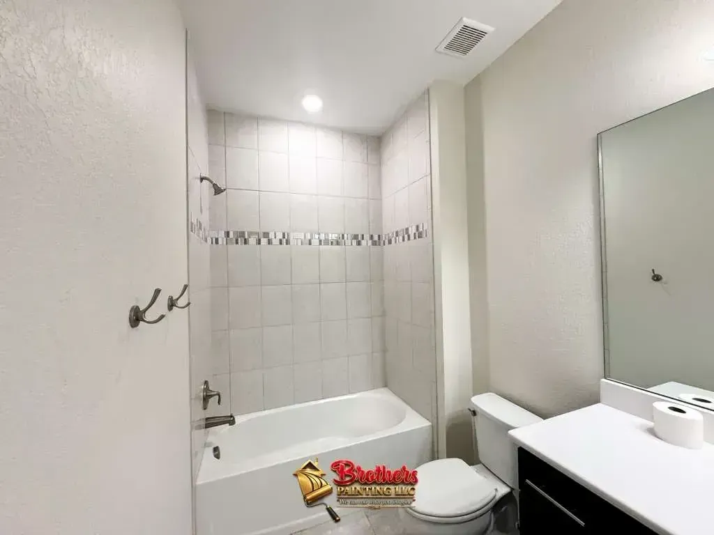 Small white bathroom with a tub, toilet, sink vanity, and wall mirror.