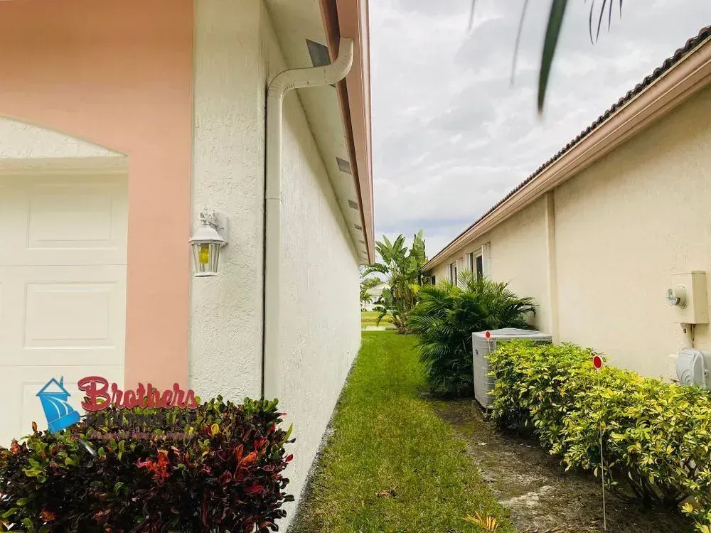 Narrow grassy walkway between two pastel houses with shrubs and a cloudy sky.