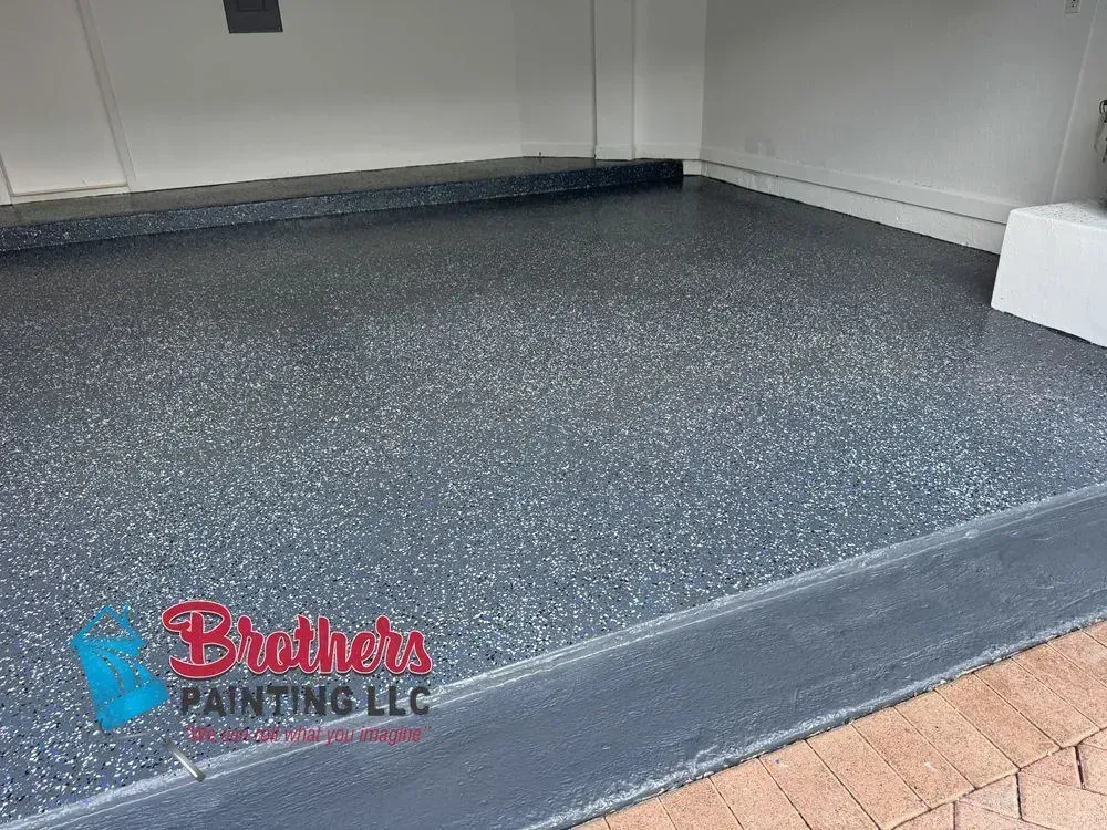 Freshly coated gray garage floor beside a brick driveway and white walls