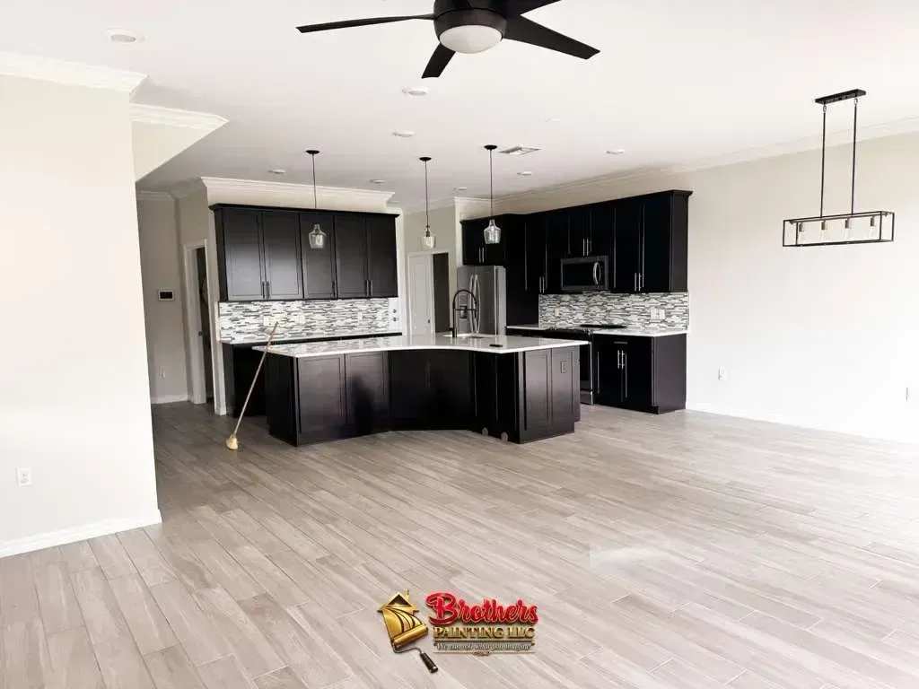 Empty modern kitchen and living area with dark cabinets, light wood floors, and a ceiling fan