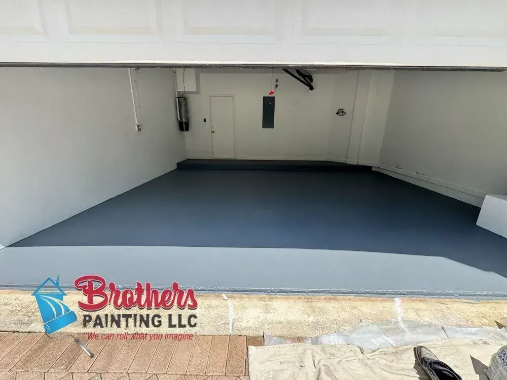 Empty garage interior with freshly painted gray floor and white walls, Brothers Painting LLC logo on the bottom left.