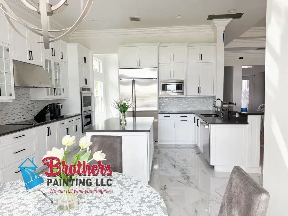 Bright white modern kitchen with marble floors, stainless steel appliances, and a glass table in the foreground