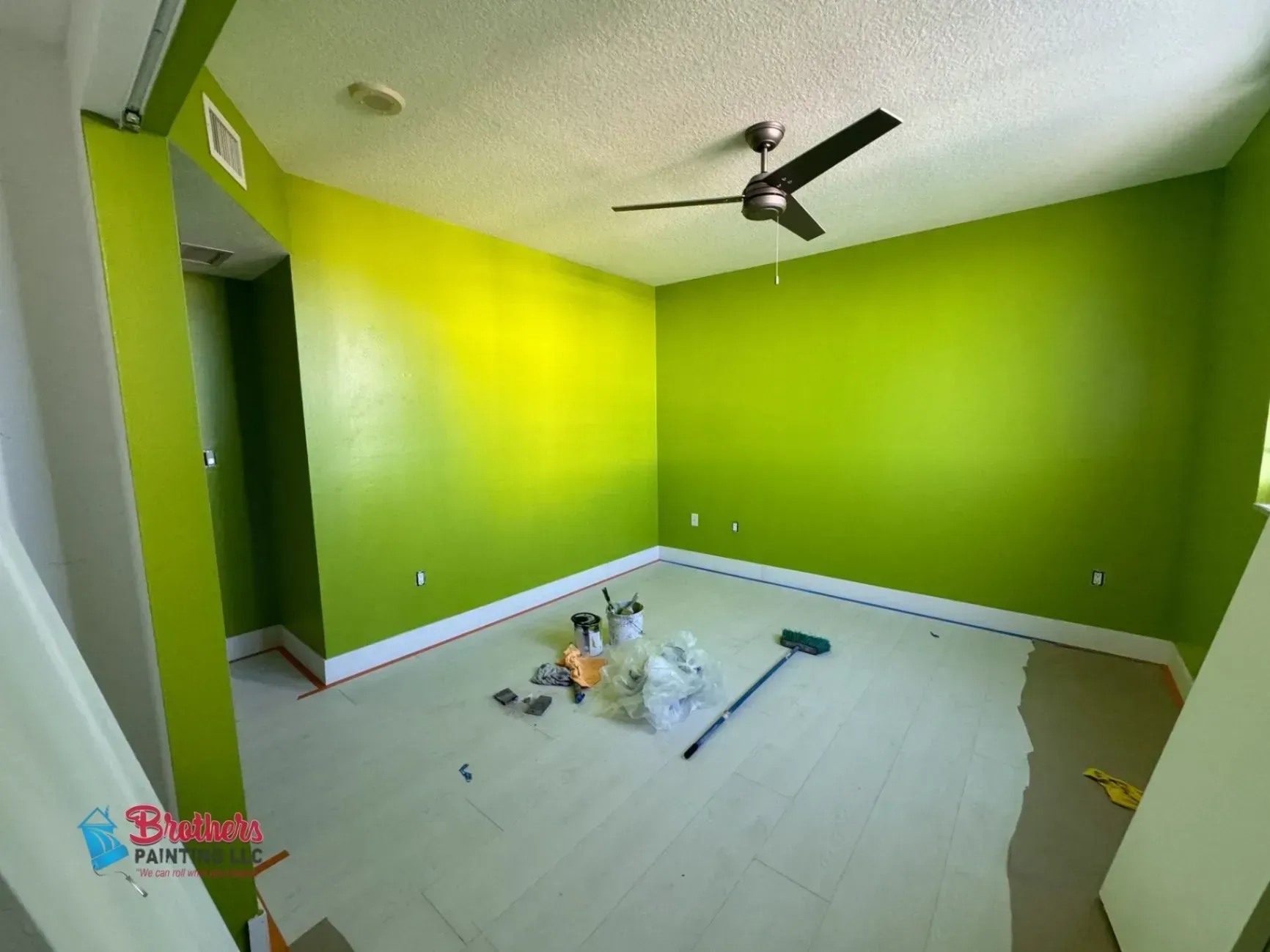 Empty room with bright green walls, white floor tiles, and a black ceiling fan.