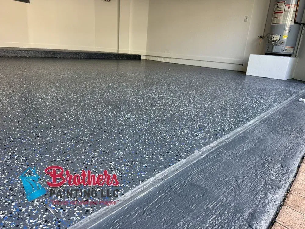 Gray speckled epoxy garage floor with a raised seam, viewed from inside an open garage