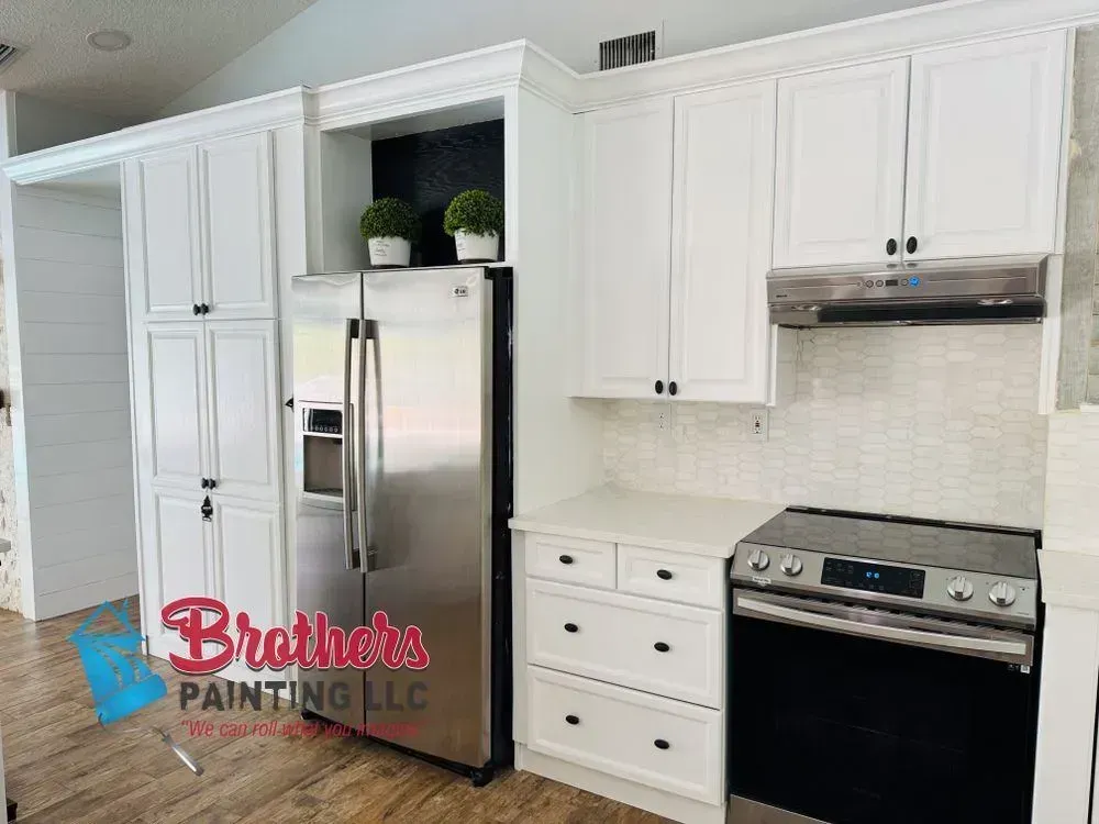 Bright white kitchen with cabinets, stainless steel refrigerator, and black stove beside a tiled backsplash