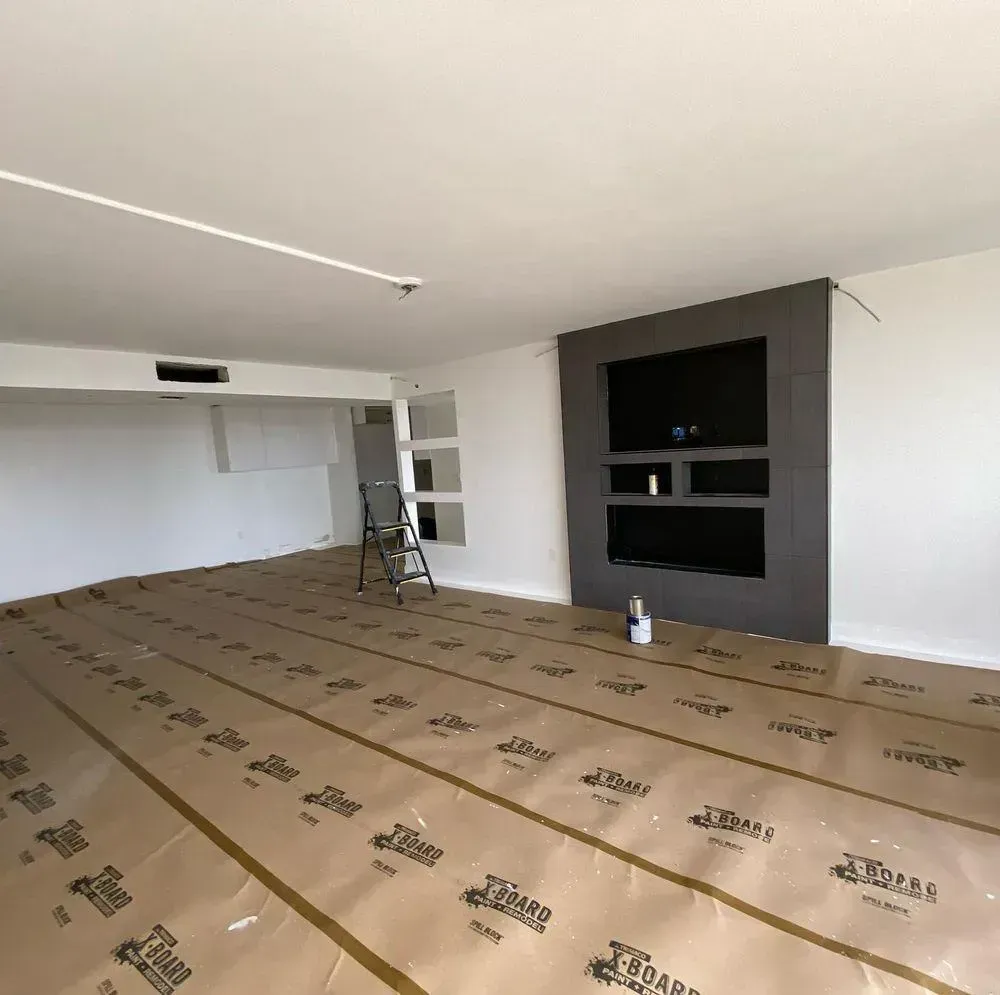 Empty living room under renovation with cardboard floor covering and a dark fireplace wall.