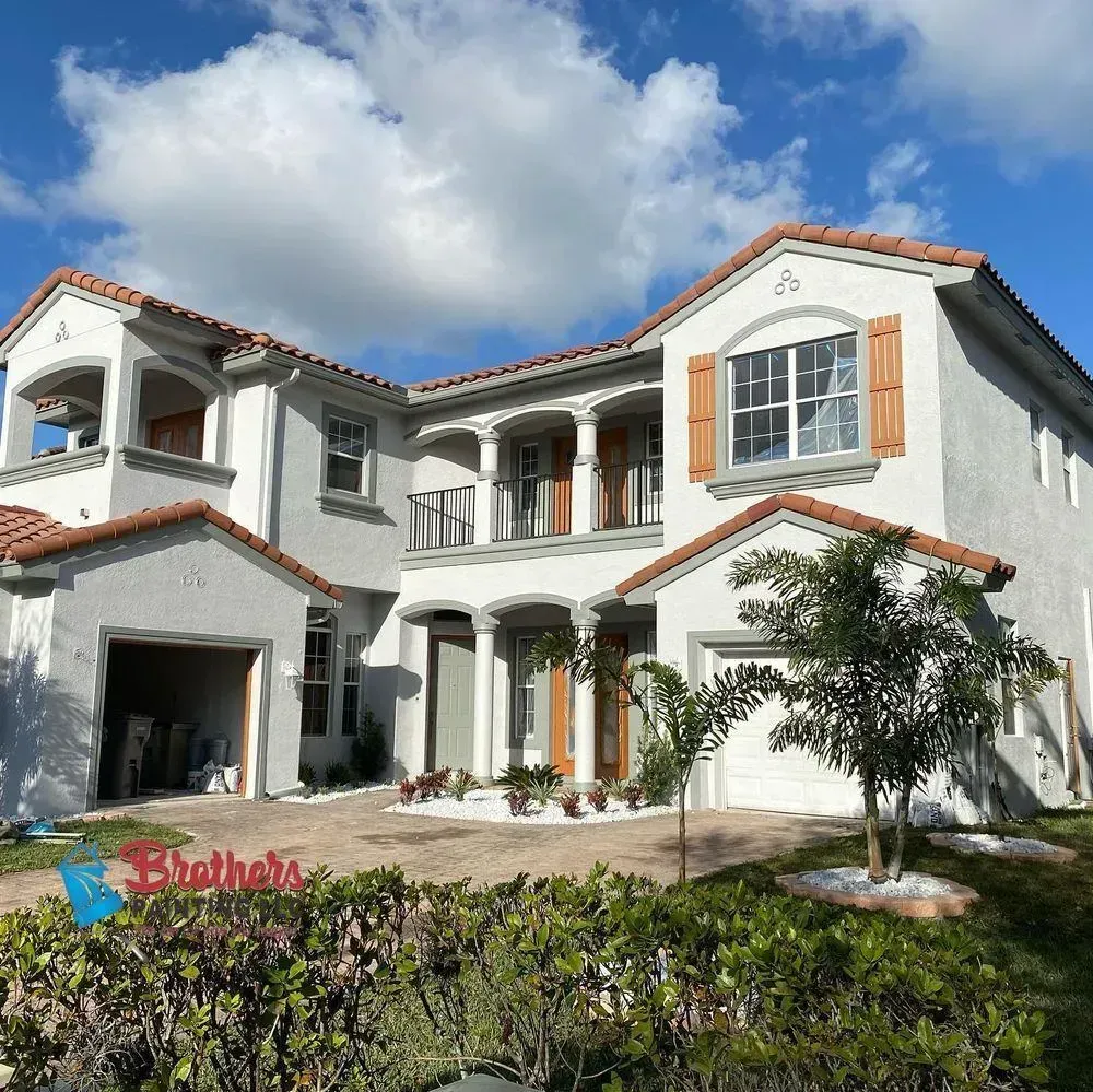 Large white two-story house with red-tiled roof, arched windows, garage, and blue sky with clouds.