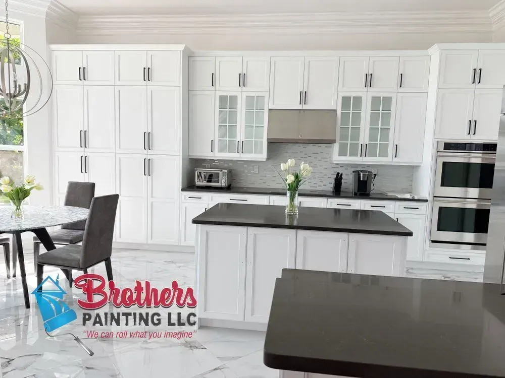 Bright white modern kitchen with black countertops and stainless appliances; Brothers Painting LLC logo visible.