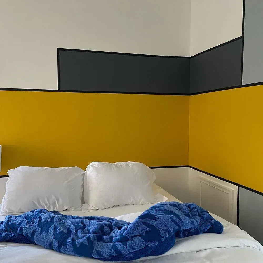 Bed with white pillows and blue blanket against a yellow and dark gray bedroom wall.