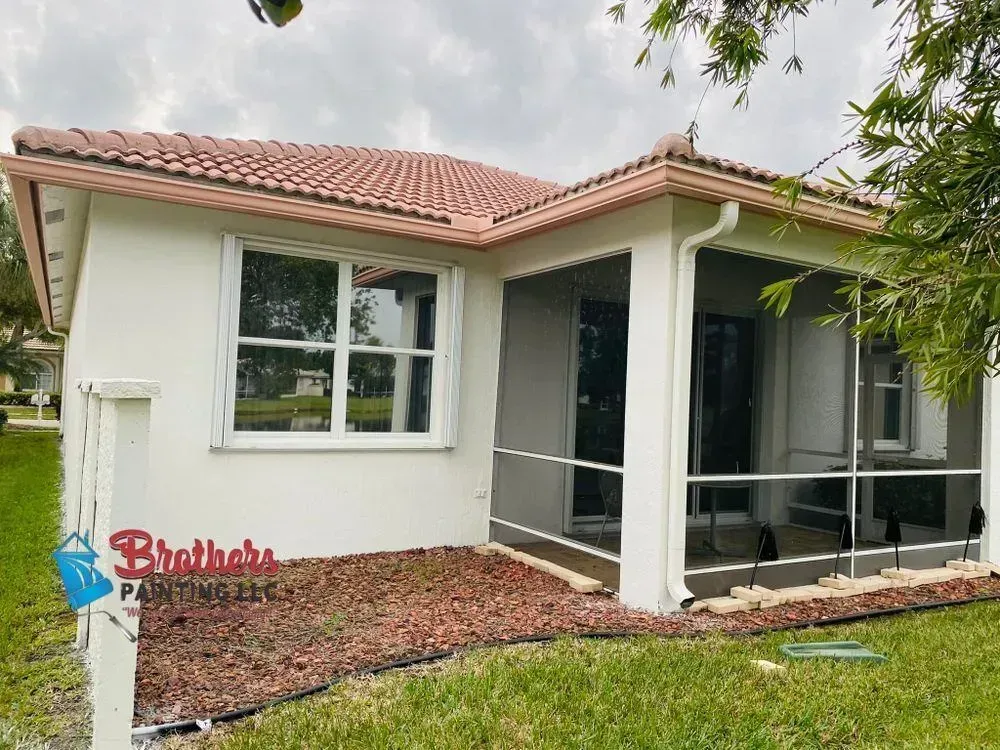 Single-story white house with red tile roof, screened patio, and small front yard