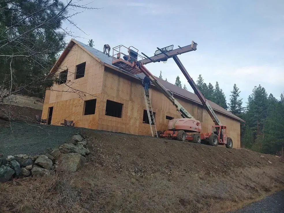 Construction workers on a roof beside a house under construction, with a crane lifting materials.