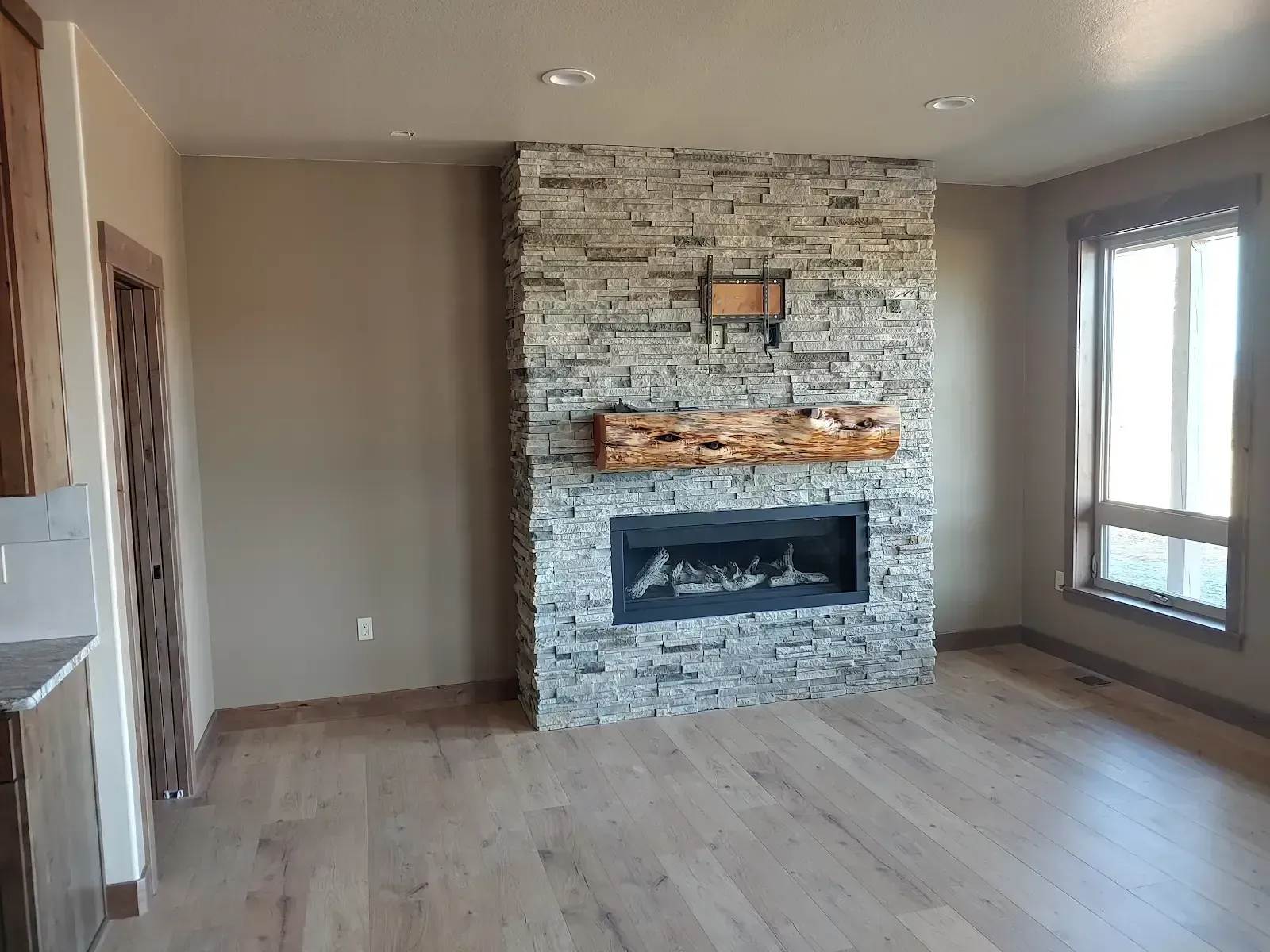 Living room with stone fireplace, hardwood floors, and large windows