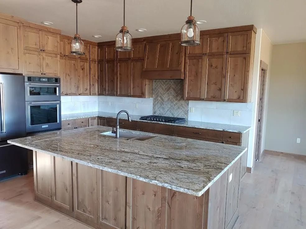 Modern kitchen with wood cabinets, granite island, stainless appliances, and pendant lights.