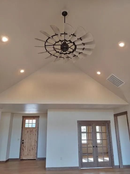 Spacious room with vaulted ceiling, large chandelier, recessed lights, wood doors, and French doors.