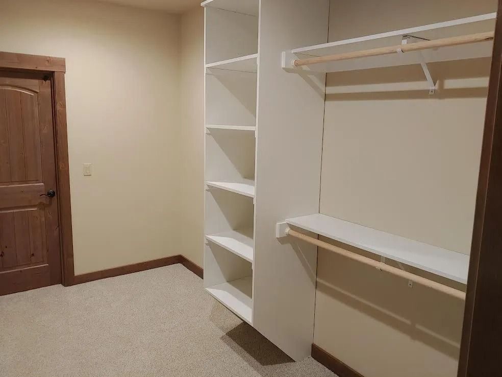 Empty walk-in closet with white shelves and hanging rods next to a wooden door.