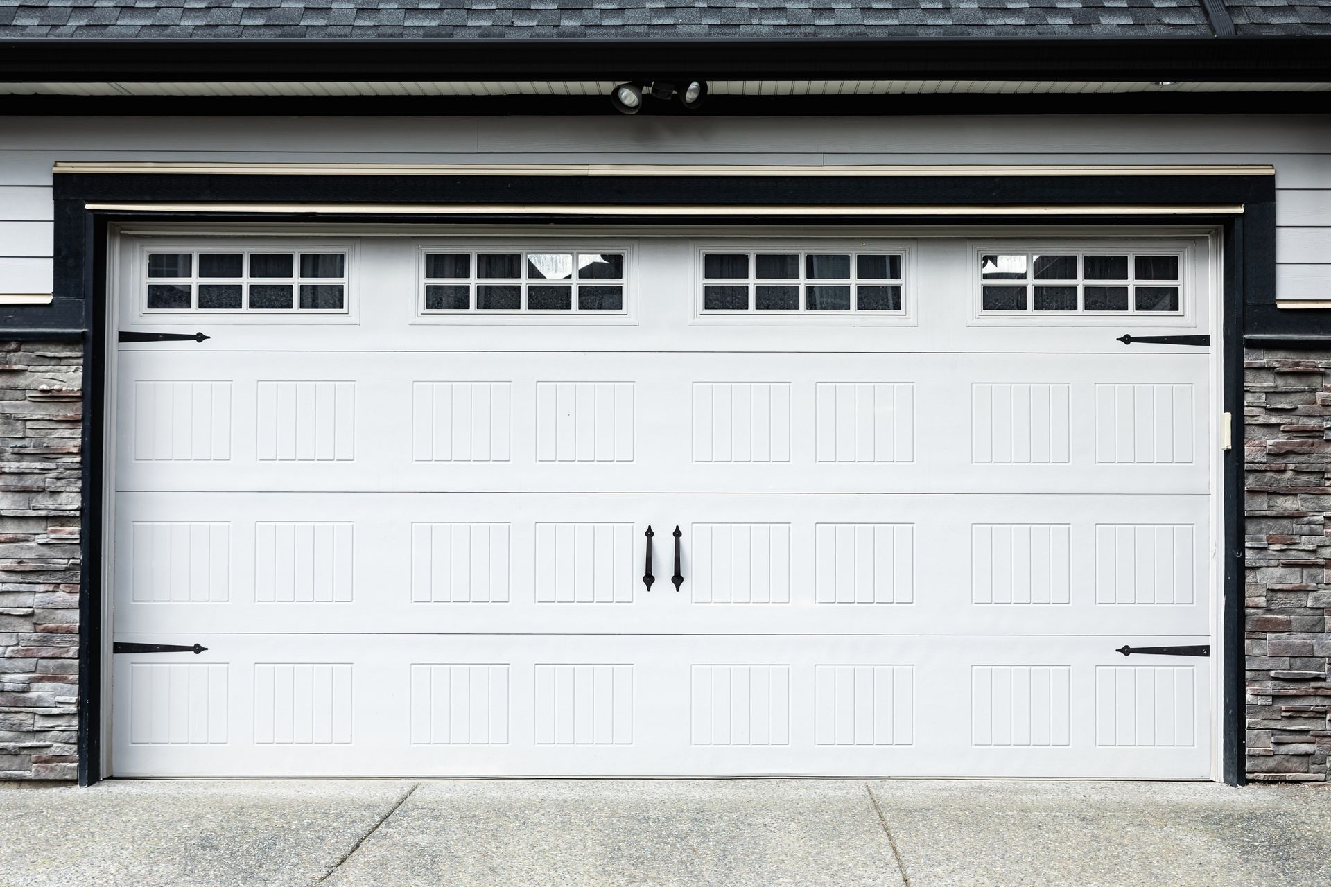 White double garage door with black handles beneath a house roofline
