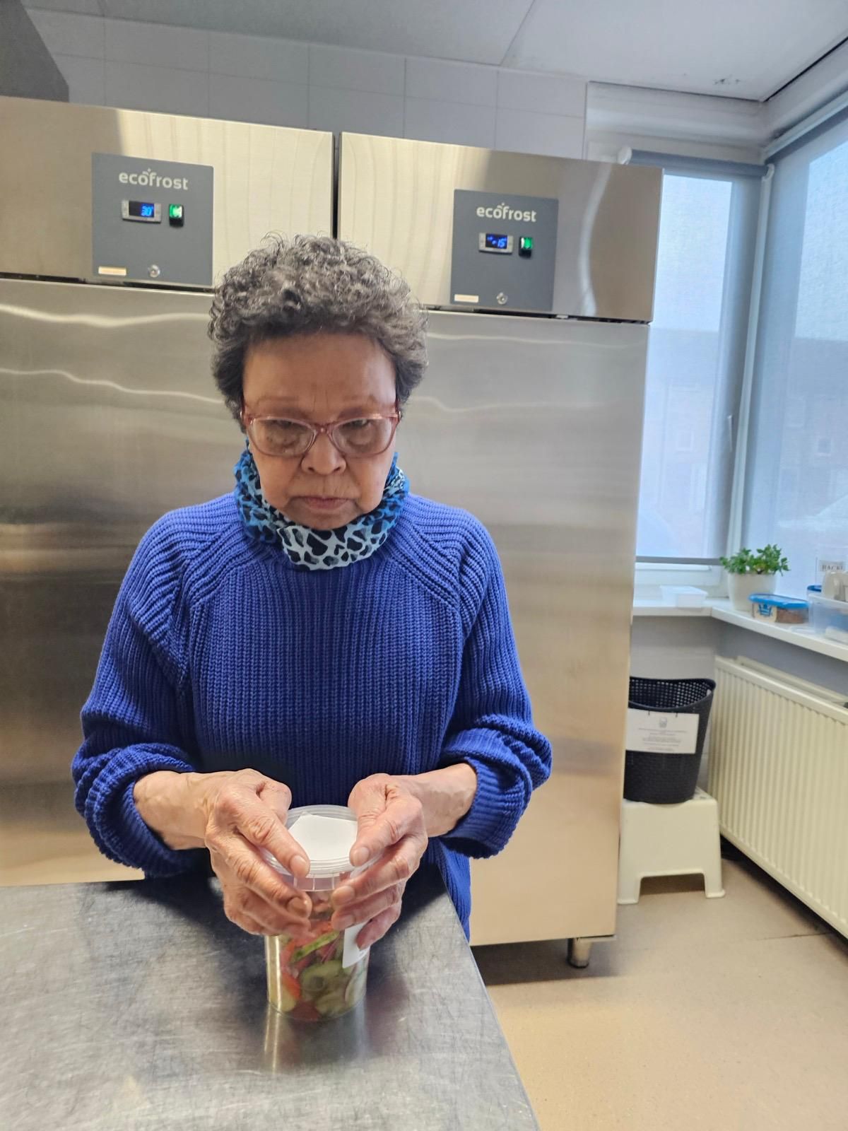 Een vrouw in een blauwe trui opent een fles in een keuken.