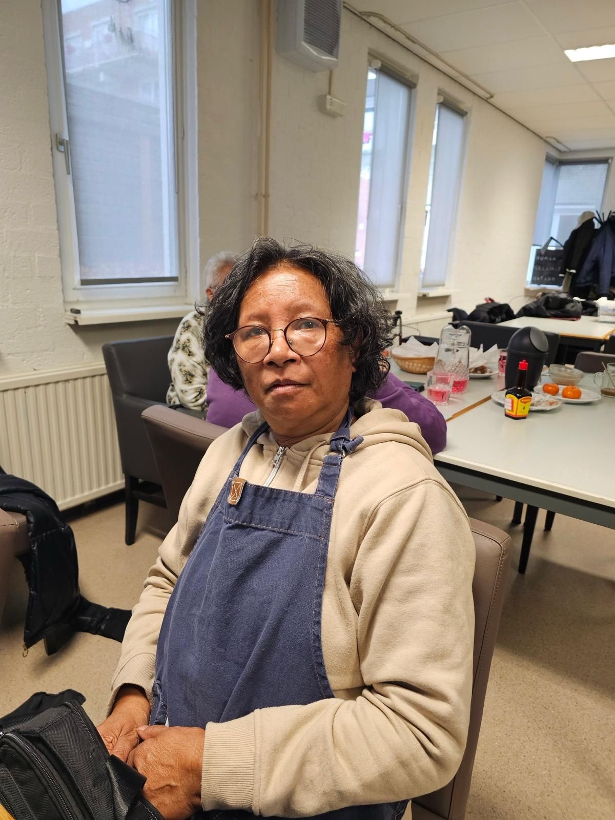 Een vrouw in een overall en een bril zit in een stoel in een kamer.