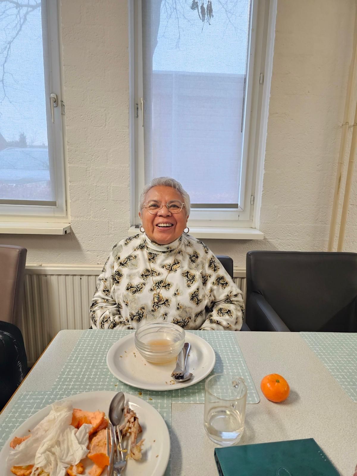 Een oudere vrouw zit aan een tafel met borden vol eten.