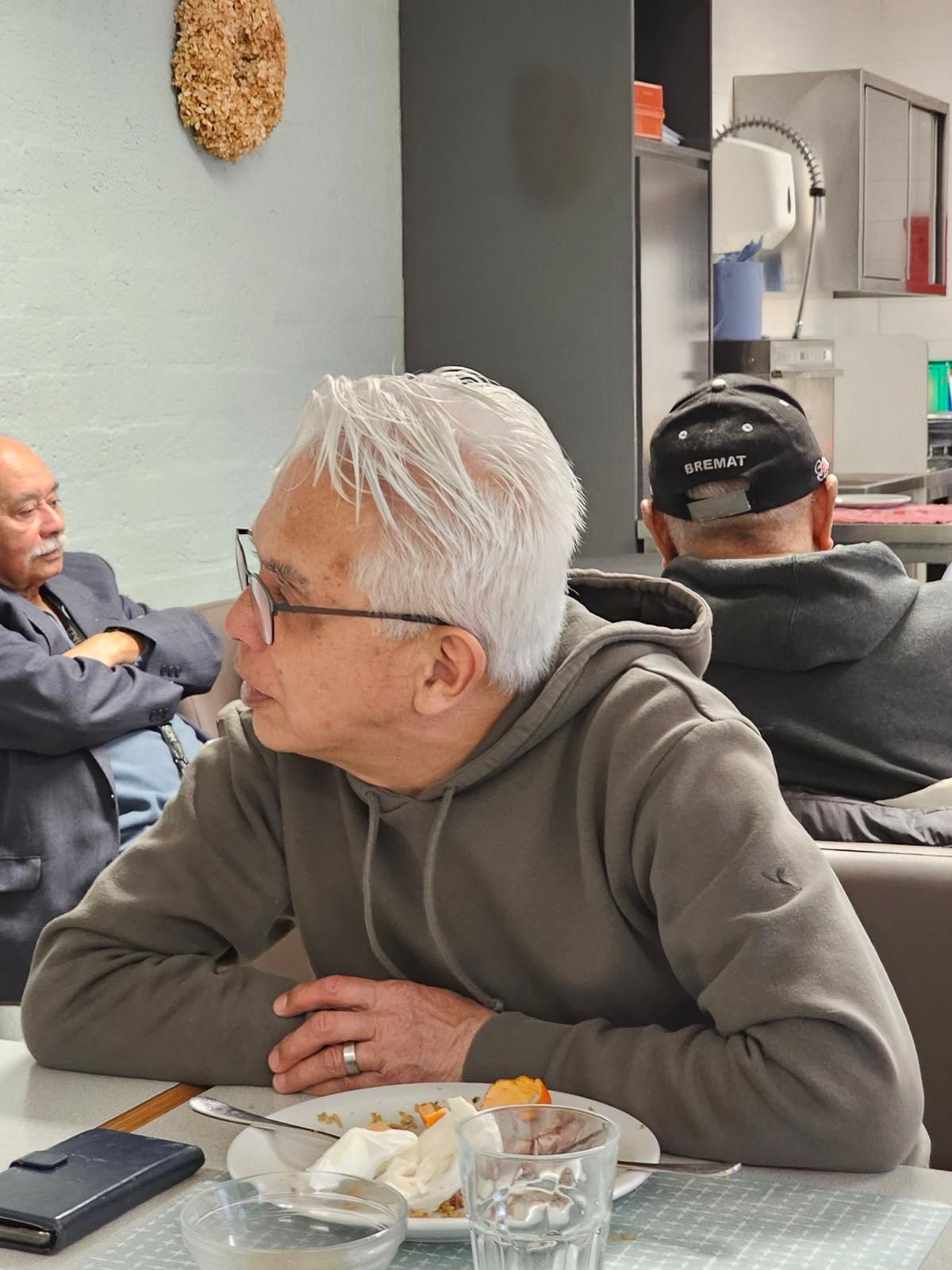 Een man met een bril zit aan een tafel met een bord eten.