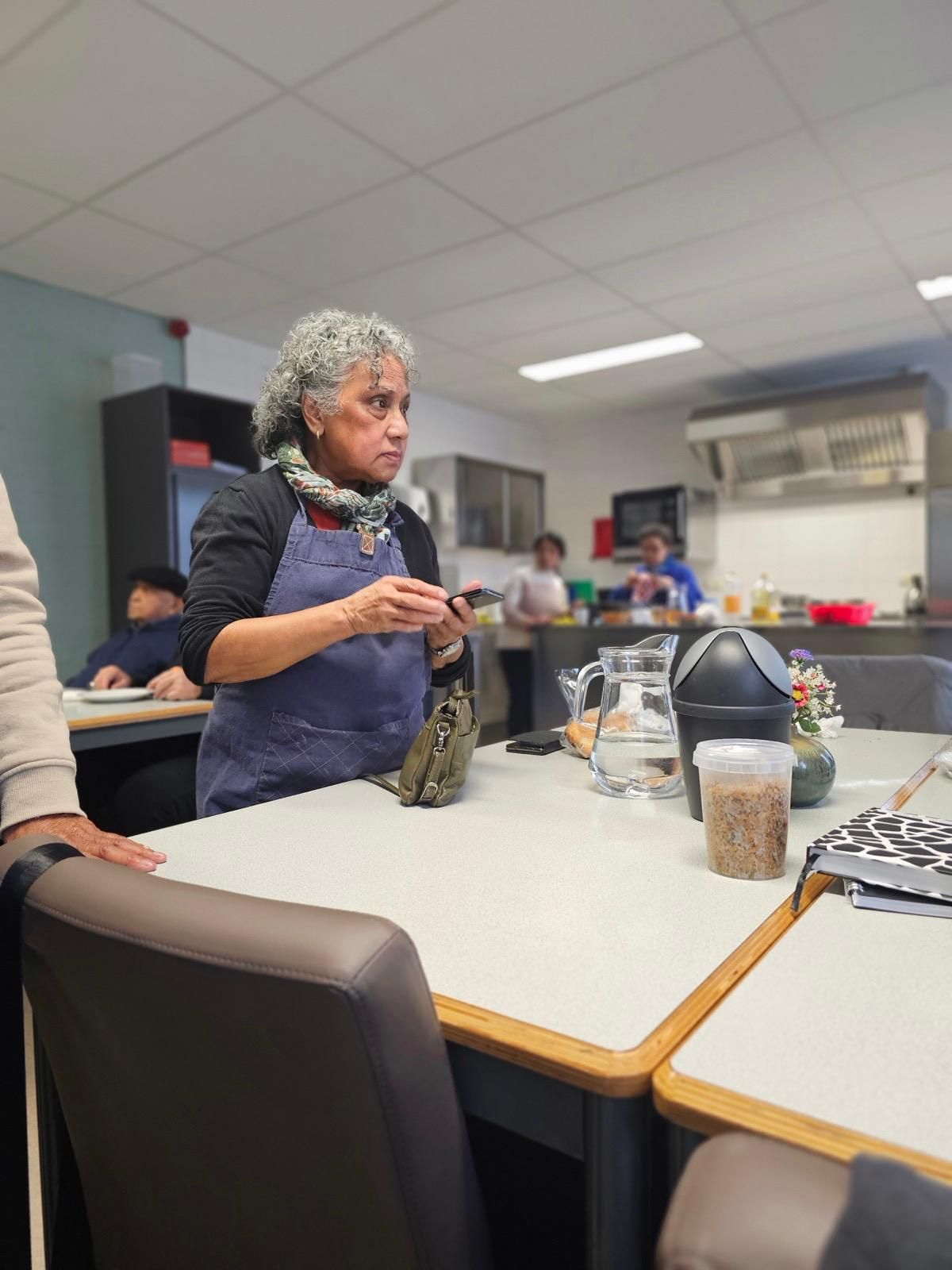 Een vrouw staat aan een tafel in een keuken en praat met een groep mensen.
