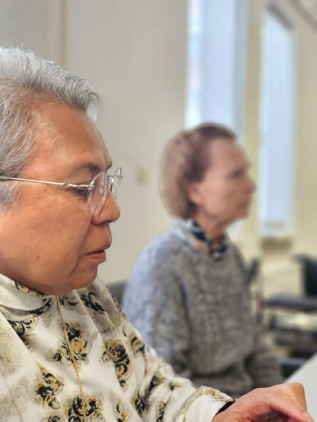 Een vrouw met een bril gebruikt een computer terwijl een andere vrouw achter haar zit