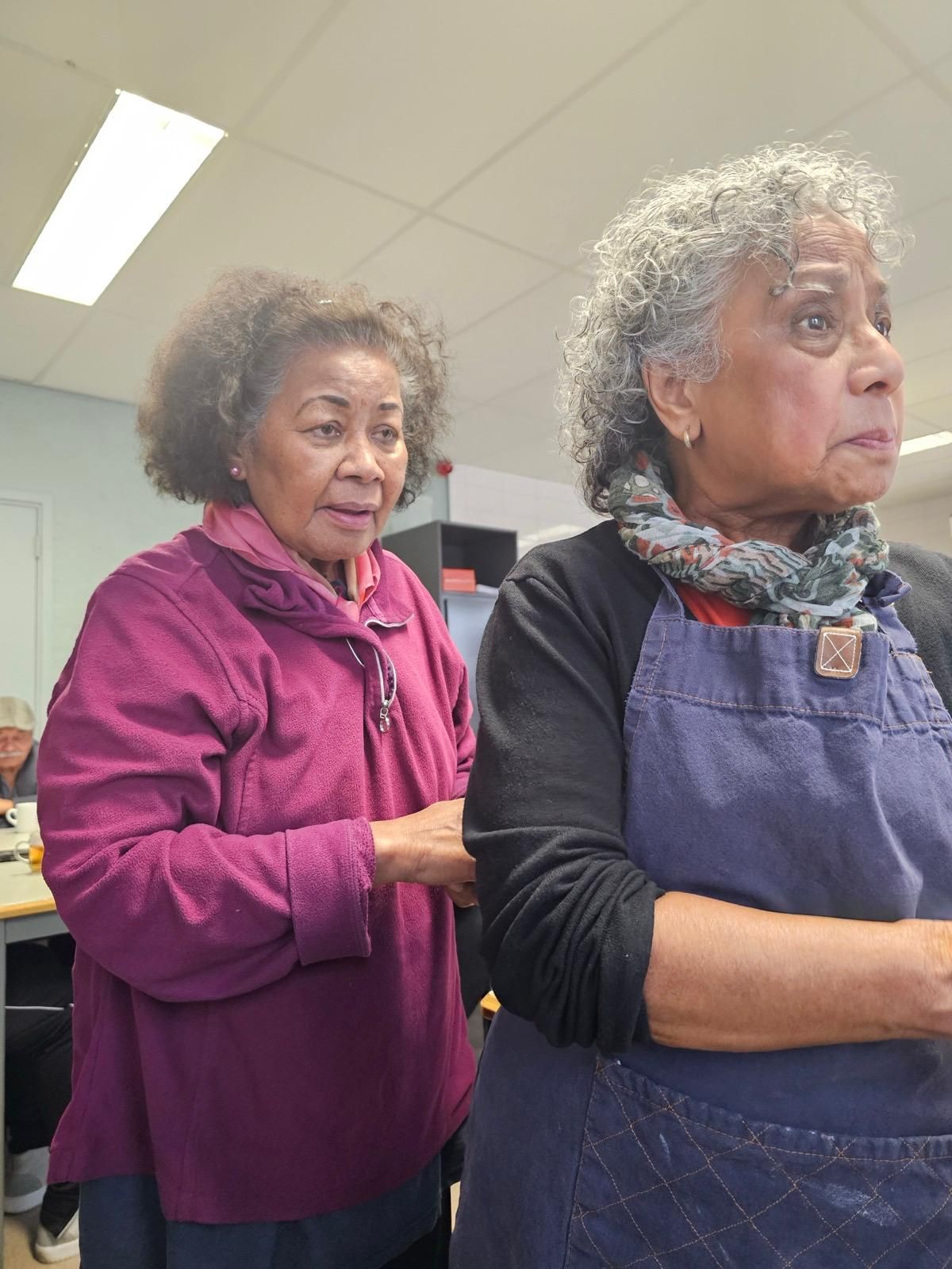 Twee oudere vrouwen staan ​​naast elkaar in een kamer.