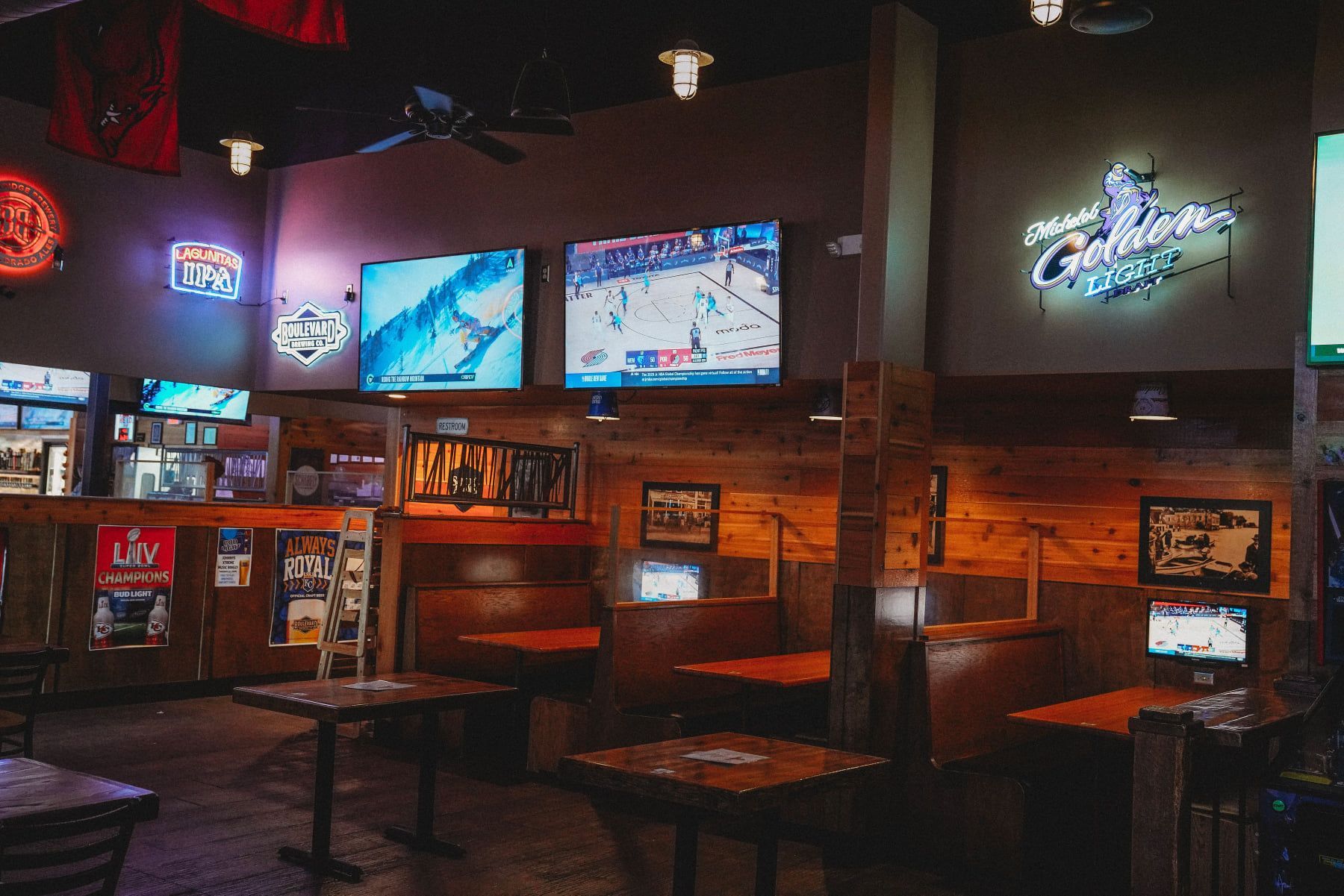 Inside a bar: Multiple TVs show sports, brown booths, neon signs, dark interior.