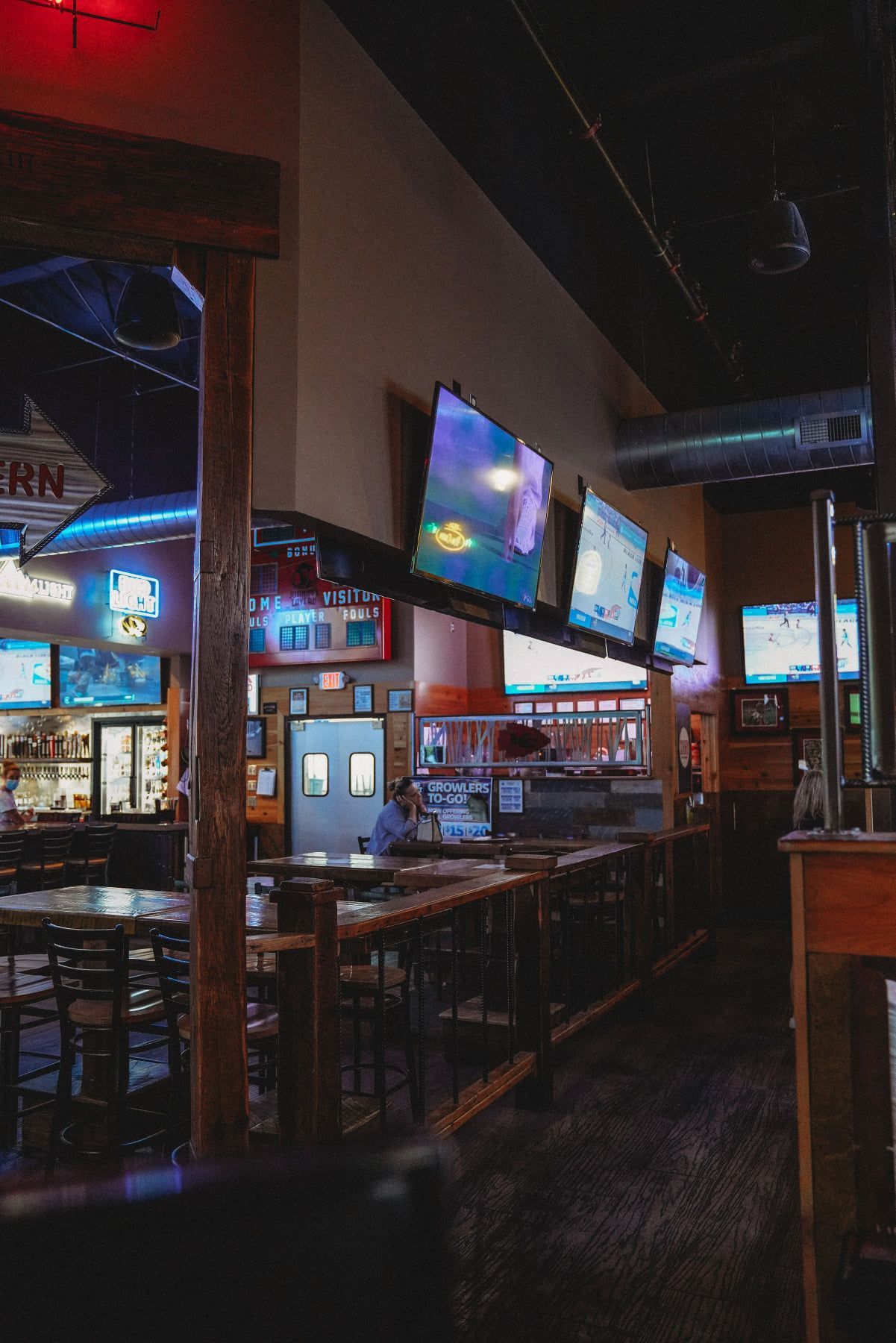 Interior of a sports bar with multiple TVs, tables, and a bar area. Dim lighting.