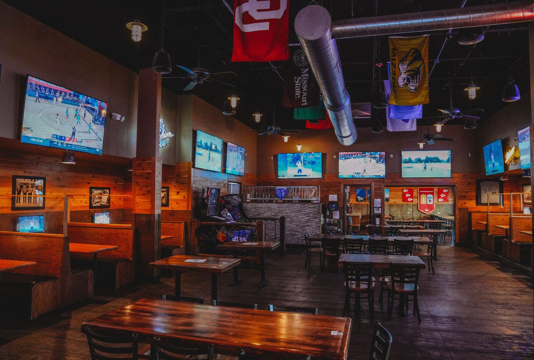 Sports bar interior with multiple TVs showing games, tables, and sports flags.
